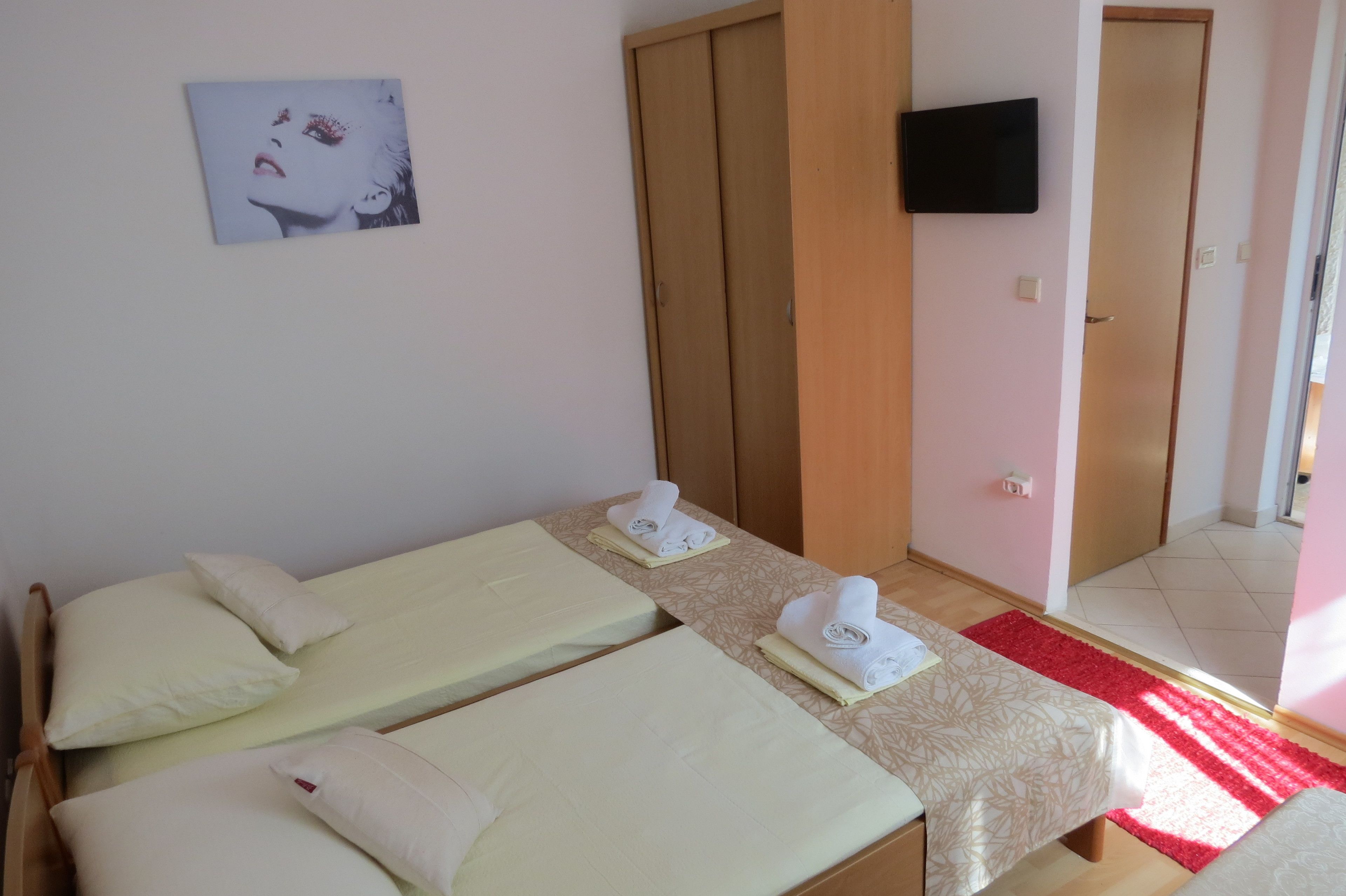A hotel room with two beds, a TV mounted on the wall, and a red rug on the floor.