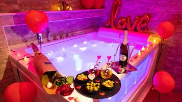 Un'atmosfera romantica con una vasca da bagno, candele, decorazioni a forma di cuore e una bottiglia di champagne.