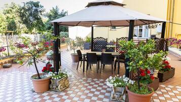Un patio esterno con zona salotto coperta, piante in vaso e pavimento piastrellato.