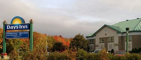 A Days Inn sign with a sun logo, surrounded by autumn foliage and a building with a green roof.