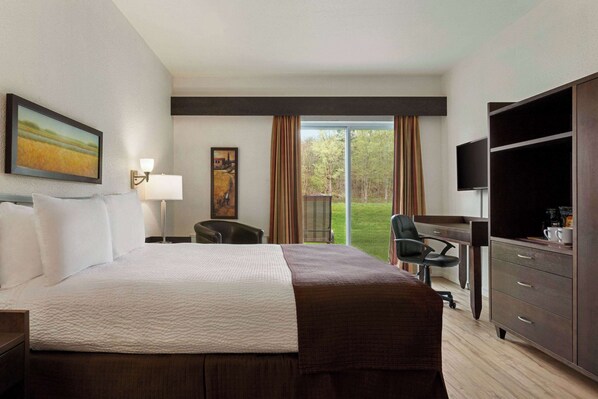 Ein Hotelzimmer mit einem großen Bett, einem Schreibtisch mit Stuhl, einem Fernseher und Blick ins Freie.