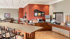 Un espace dédié au petit-déjeuner, avec une longue table, des chaises, une machine à café et un présentoir où sont exposés différents aliments.