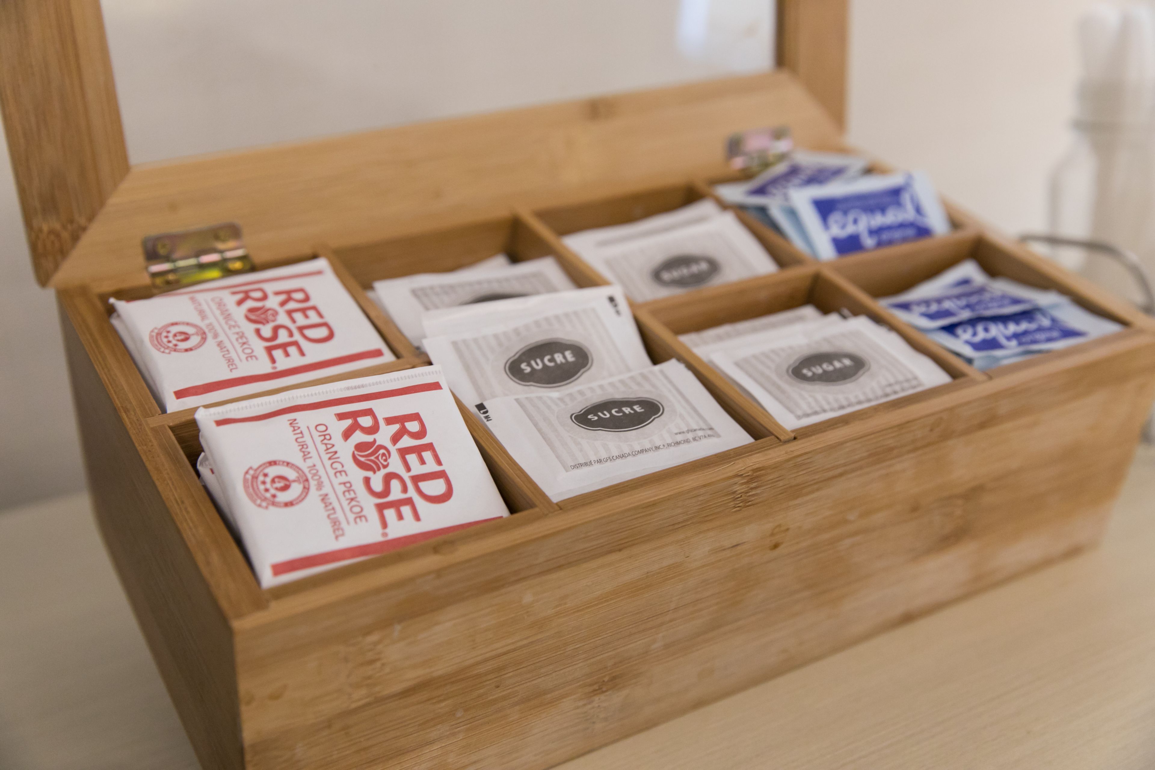Una caja de madera con compartimentos que contienen varios paquetes etiquetados como 'Red Rose' y 'Sucre'.