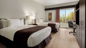 Une chambre d’hôtel avec deux lits, un bureau, une chaise et une grande fenêtre donnant sur les arbres.