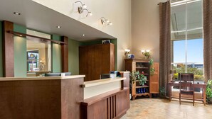 Un espace d’accueil comprenant un comptoir de réception en bois, un grand miroir et un coin salon avec une chaise et une petite table.