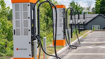 A row of KEMPPOWER electric vehicle charging stations in a parking lot.