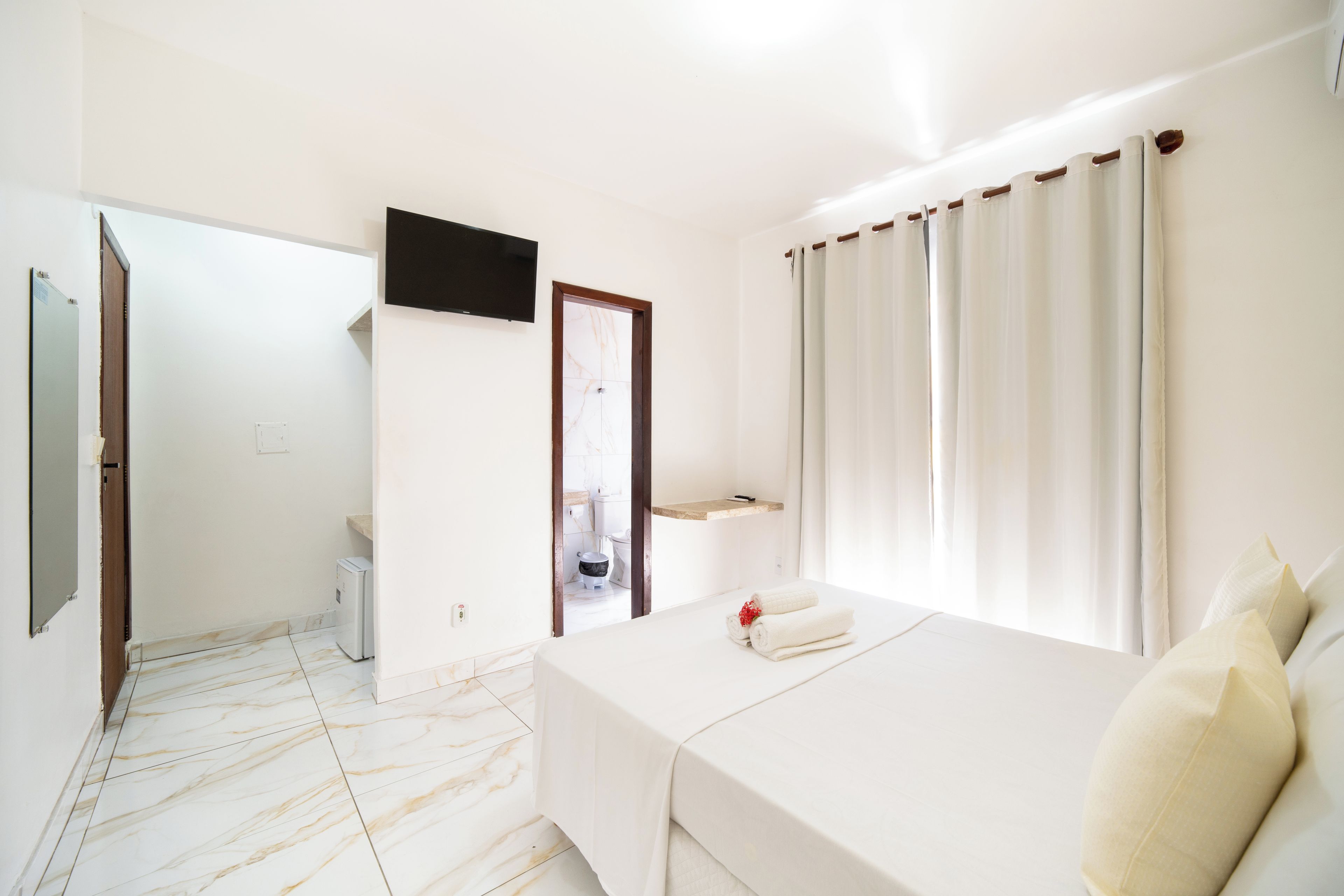 A hotel room with a bed, a television, a bathroom, and a view of the outside.