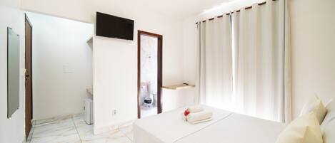 A hotel room with a bed, a television, a bathroom, and a view of the outside.