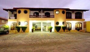 Um hotel com fachada simétrica, grandes janelas circulares e estacionamento à frente.