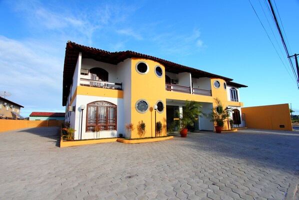 A two-story building with a yellow facade, multiple windows, and a paved courtyard. - Andimar Hotel (Porto Seguro)