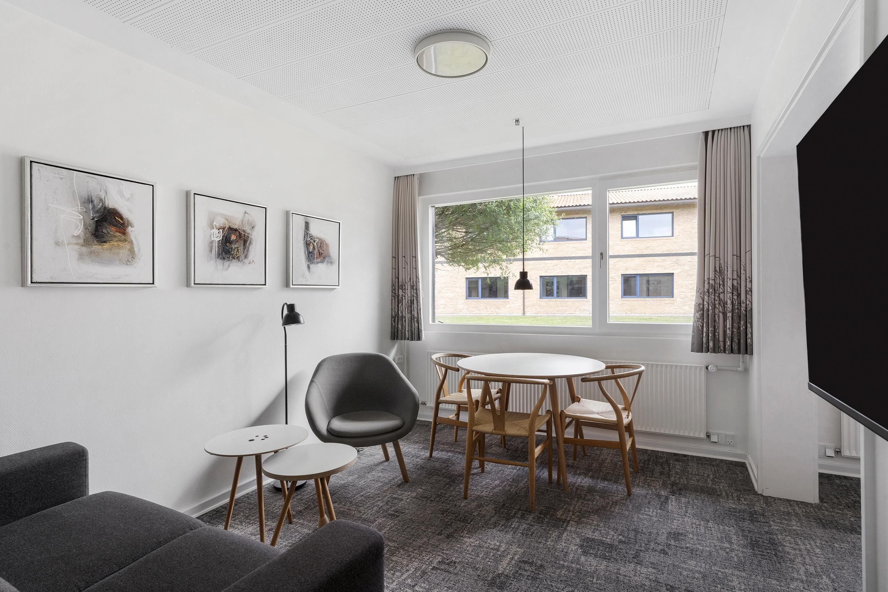 A modern room with a round table, chairs, a sofa, and artwork on the wall.