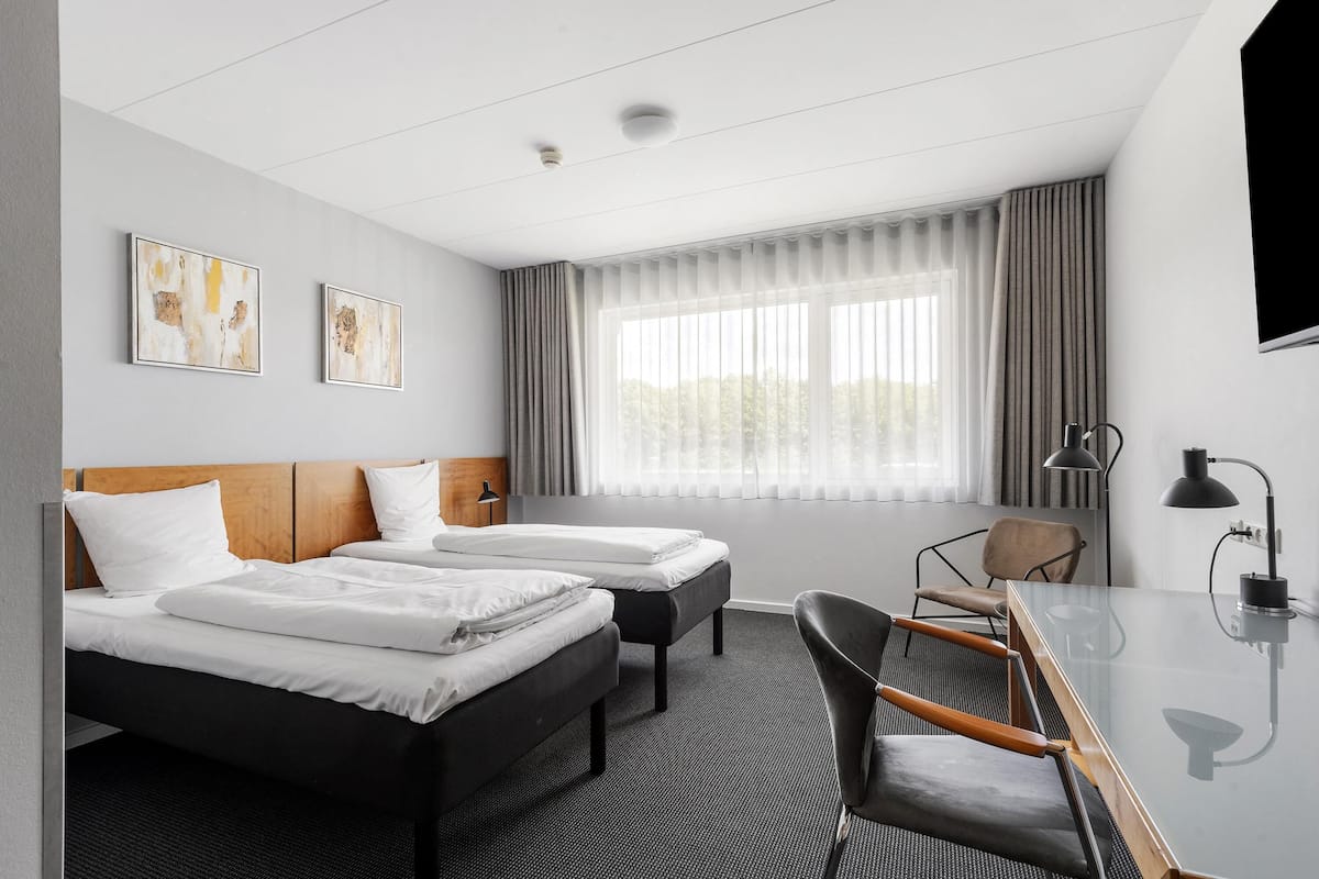 Ein Hotelzimmer mit zwei Betten, einem Schreibtisch, einem Sessel, einem Fernseher und Kunstwerken an der Wand.