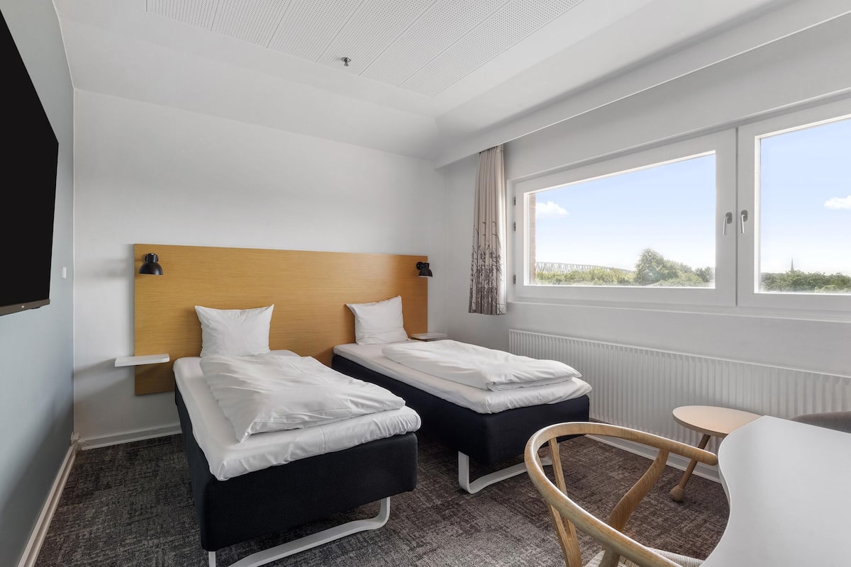 Ein Hotelzimmer mit zwei Einzelbetten, einem kleinen Tisch, einem Stuhl und einem großen Fenster mit Blick.