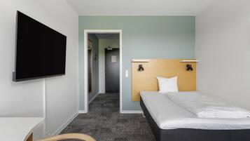 A hotel room with a bed, a TV mounted on the wall, a desk, and a chair.