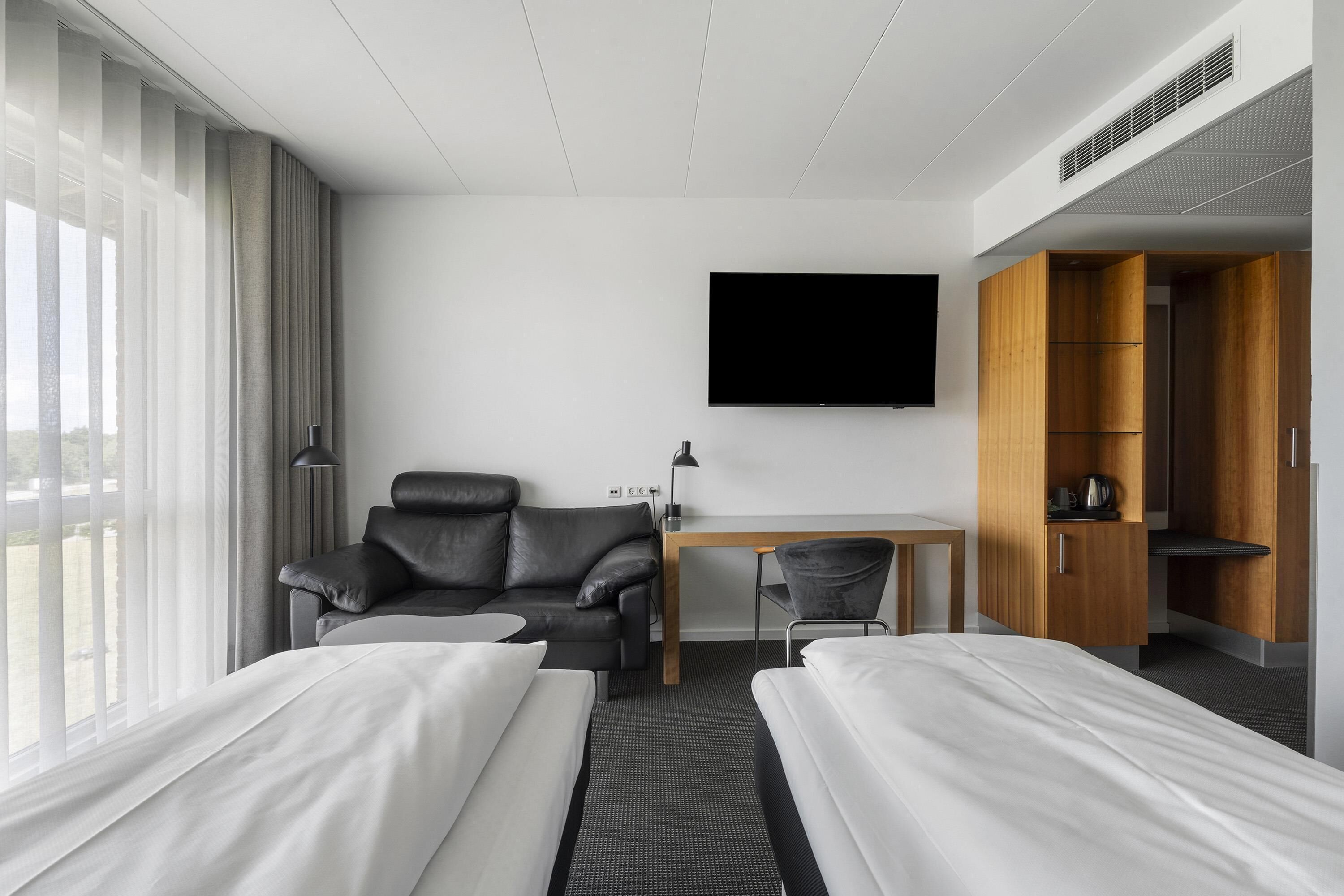 Een hotelkamer met twee bedden, een bureau, een televisie, een leren bank en een kledingkast.