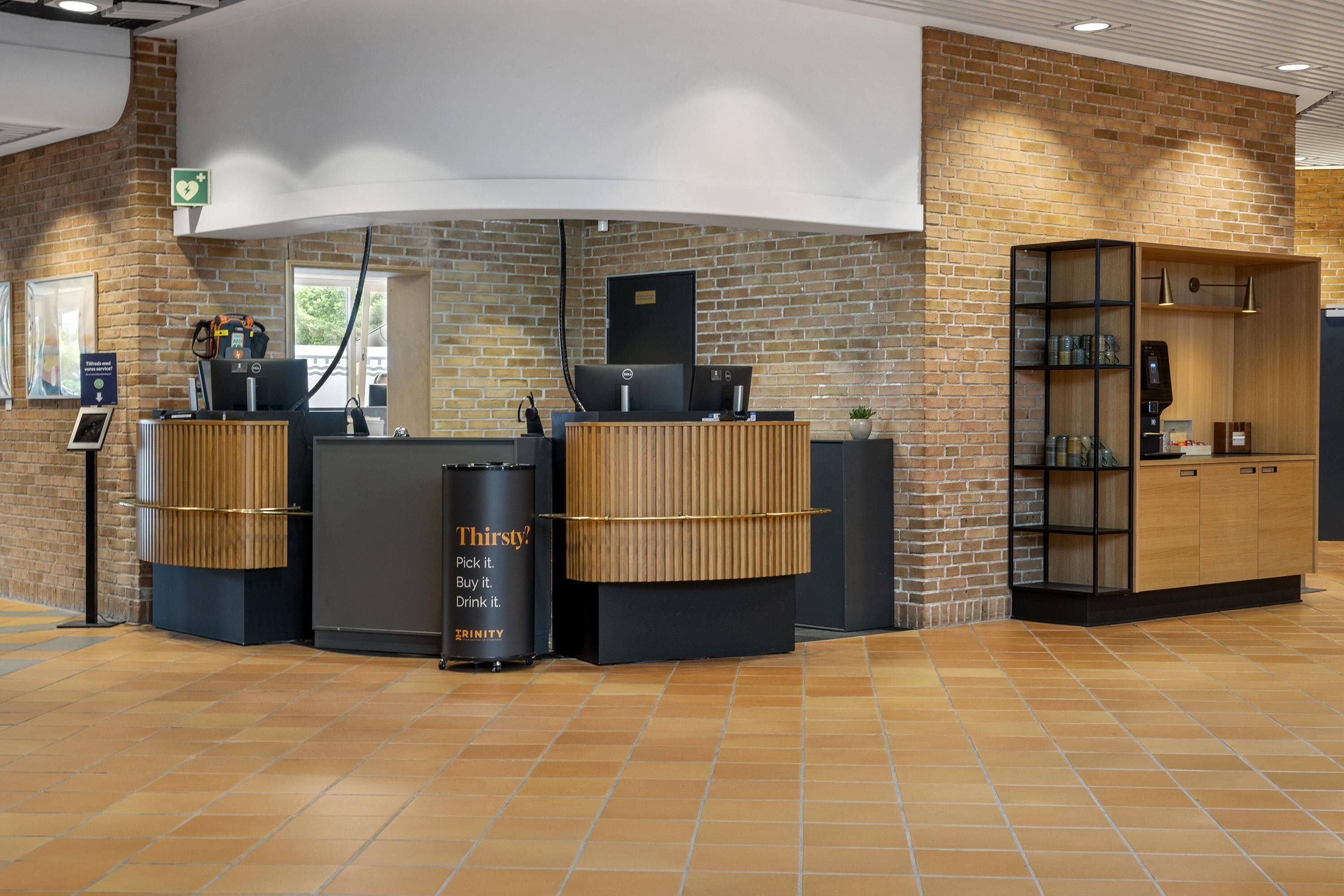 A modern reception area with a brick wall, a reception desk, a trash bin, and a wooden cabinet with shelves.