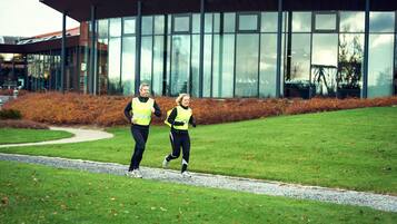 Two people jogging on a path in front of a modern building with large windows.