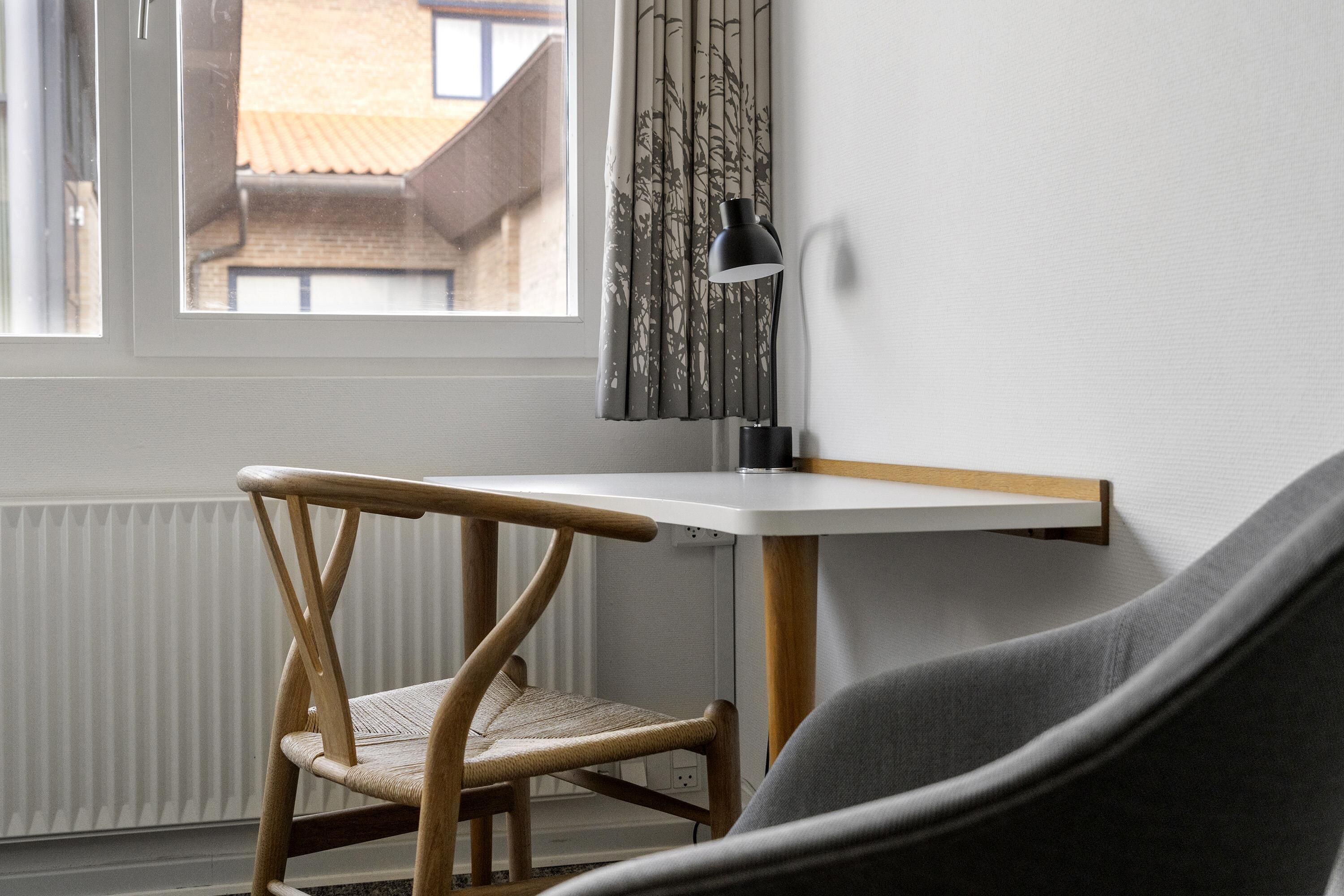 Een kamer met raam, bureau, stoel, lamp en radiator.