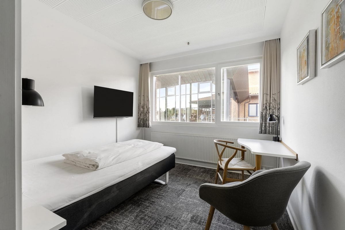 Ein modernes Hotelzimmer mit Bett, Schreibtisch, Sessel, Fernseher und großem Fenster.