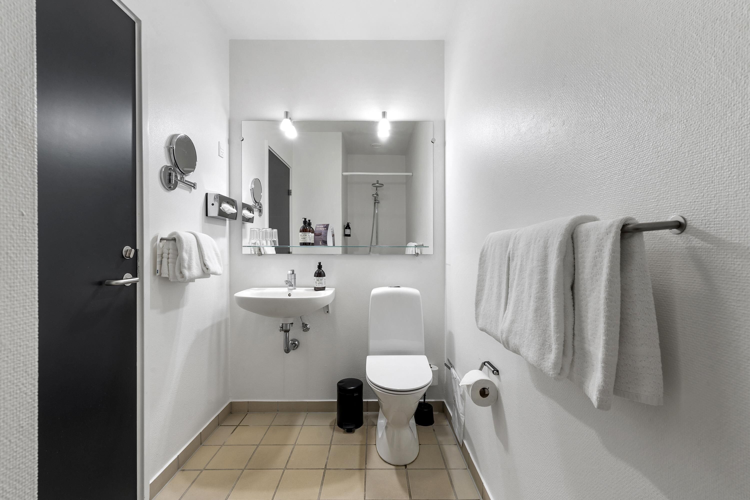 A modern bathroom with a toilet, sink, mirror, and towel rack.