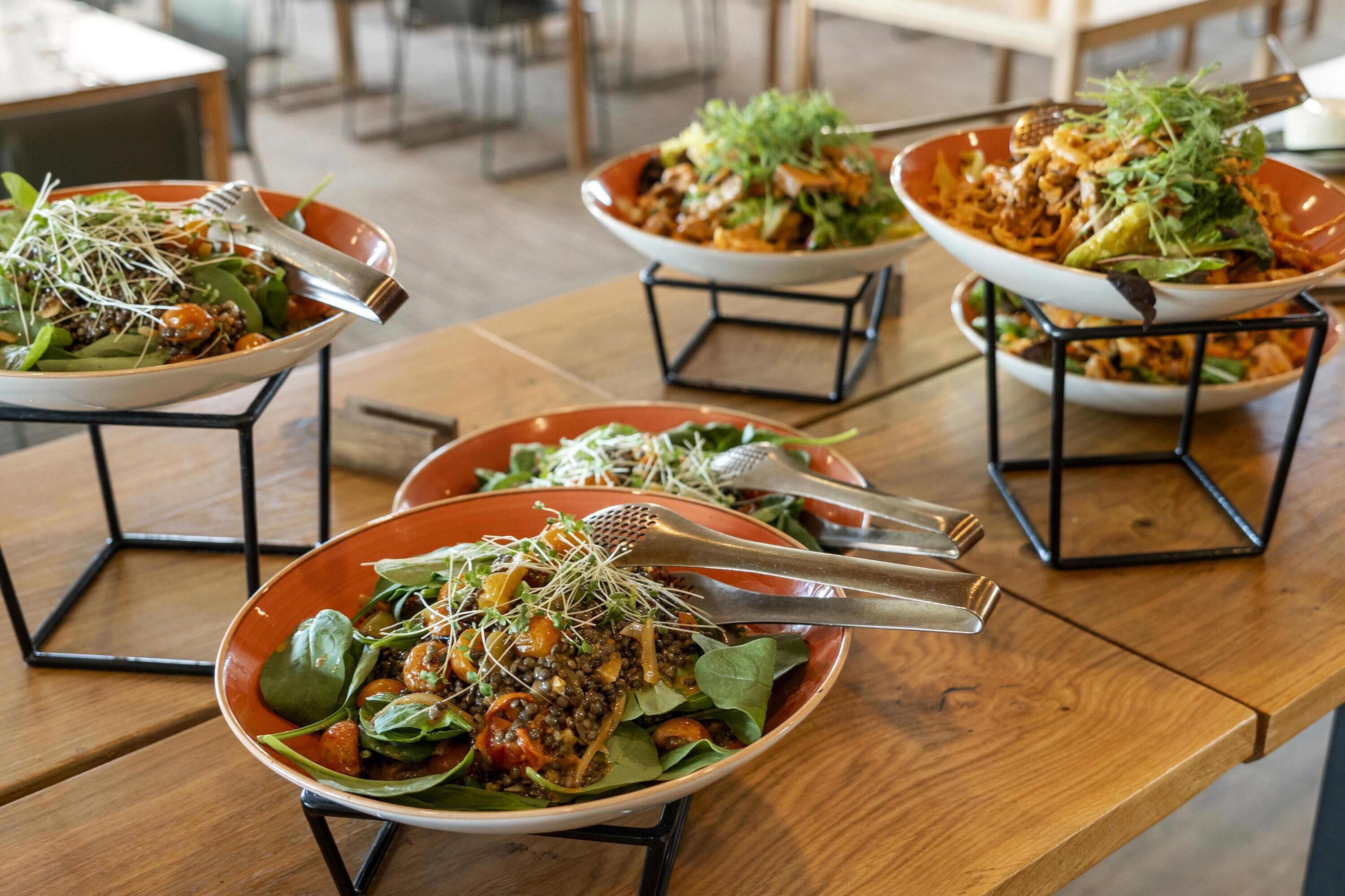 A dining table with multiple bowls of salad, each with a fork and knife.