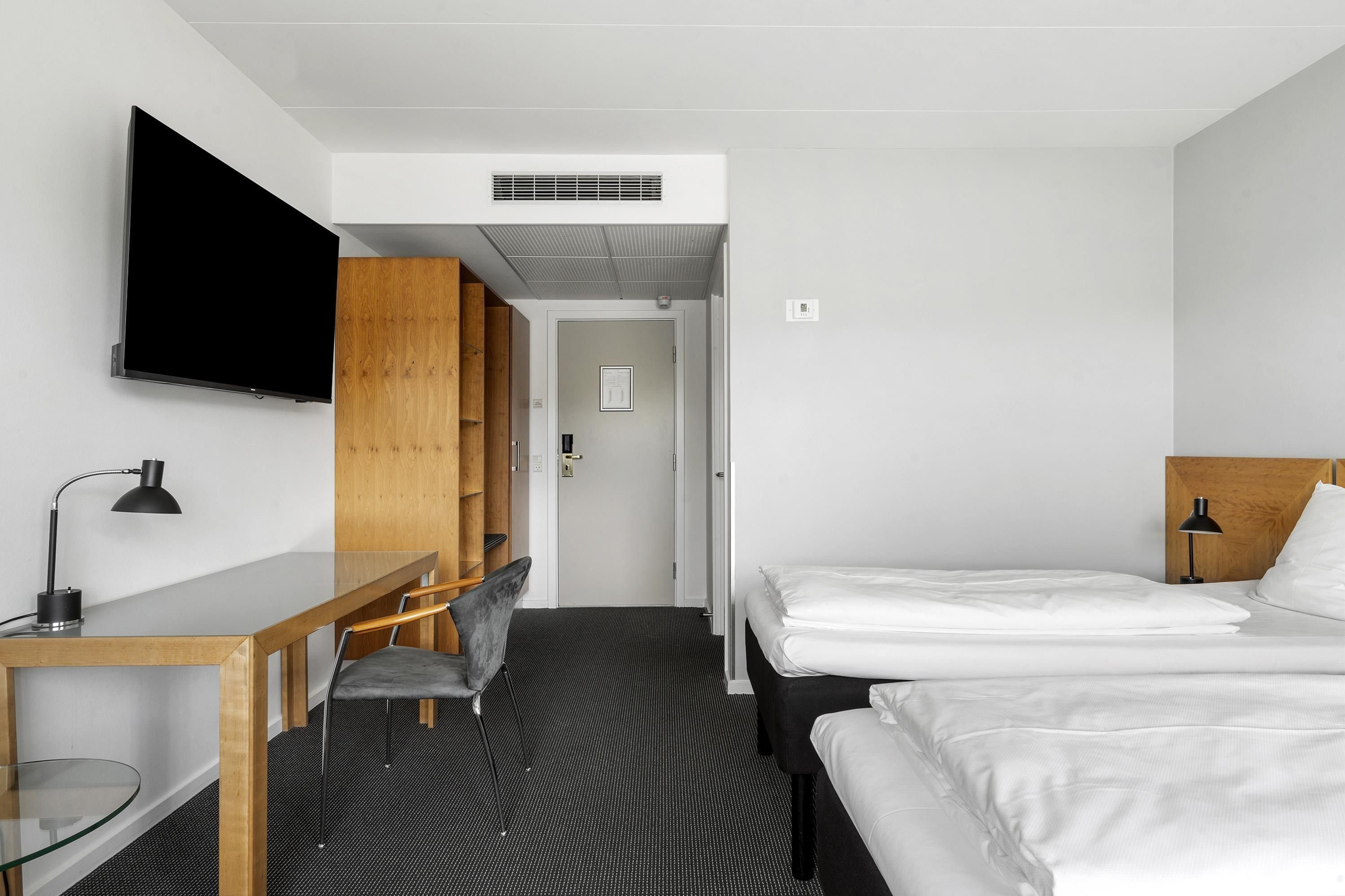 A hotel room with a bed, a desk, a chair, a TV, and a wardrobe.