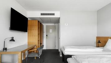 A hotel room with a bed, a desk, a chair, a TV, and a wardrobe.