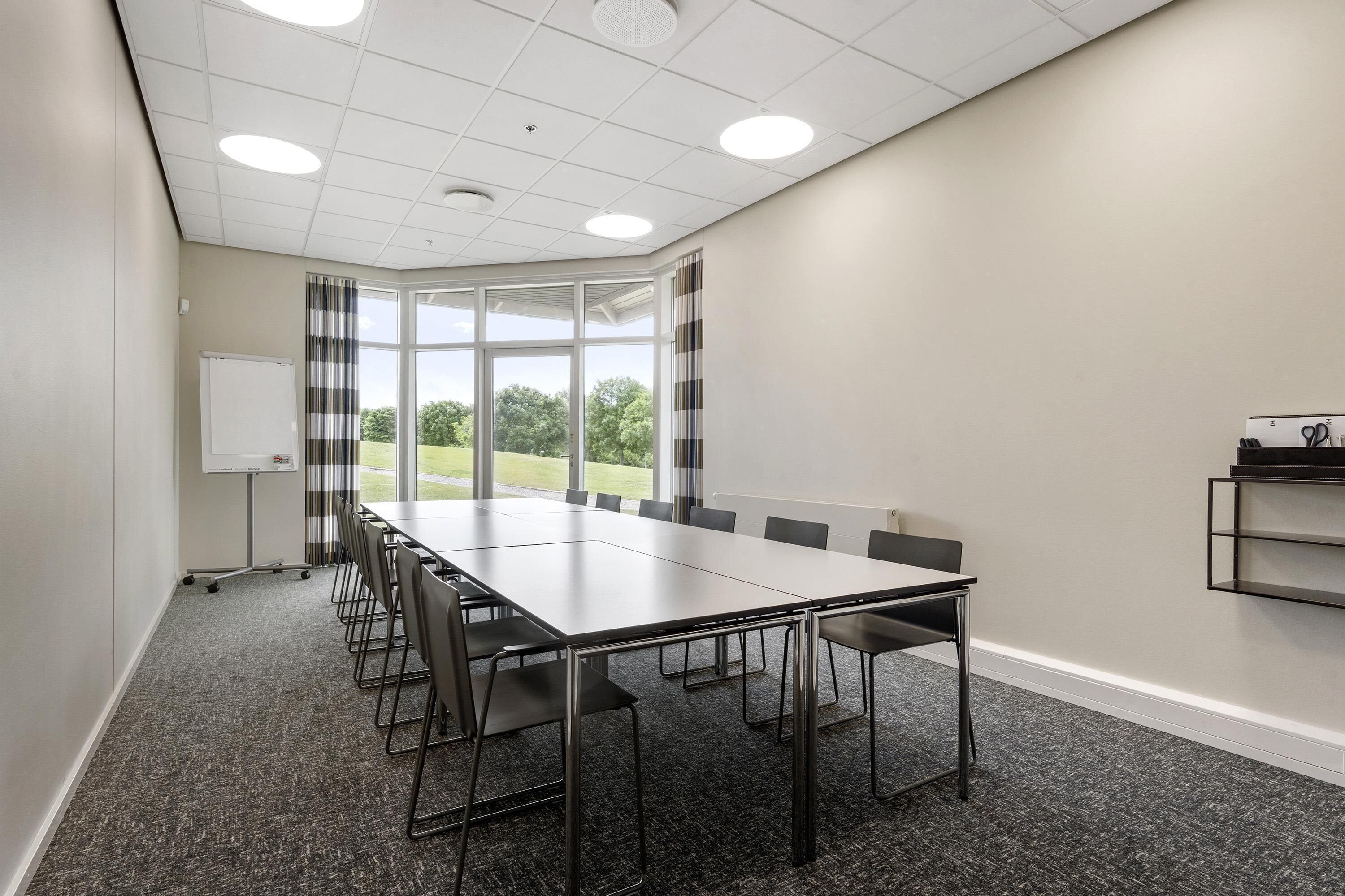 Une salle de conférence avec une longue table, des chaises, un tableau blanc et une fenêtre avec des rideaux.