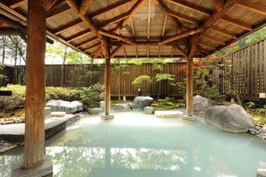 A covered outdoor hot spring area with wooden beams, rocks, and a wooden fence. - Ryotei Hanayura Ryokan (Noboribetsu)