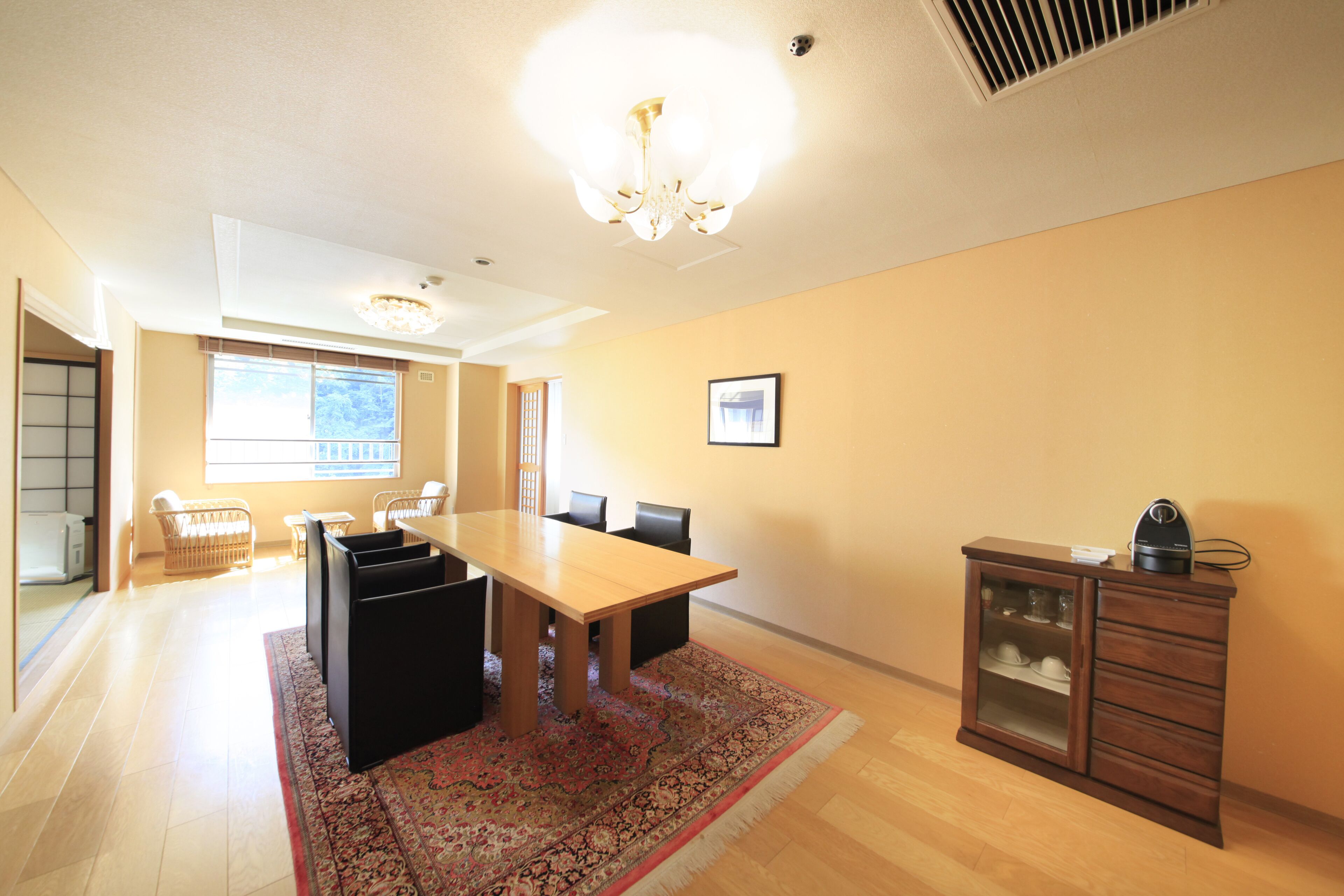 A spacious dining area with a wooden table and chairs, a patterned rug, and a cabinet with dishes.