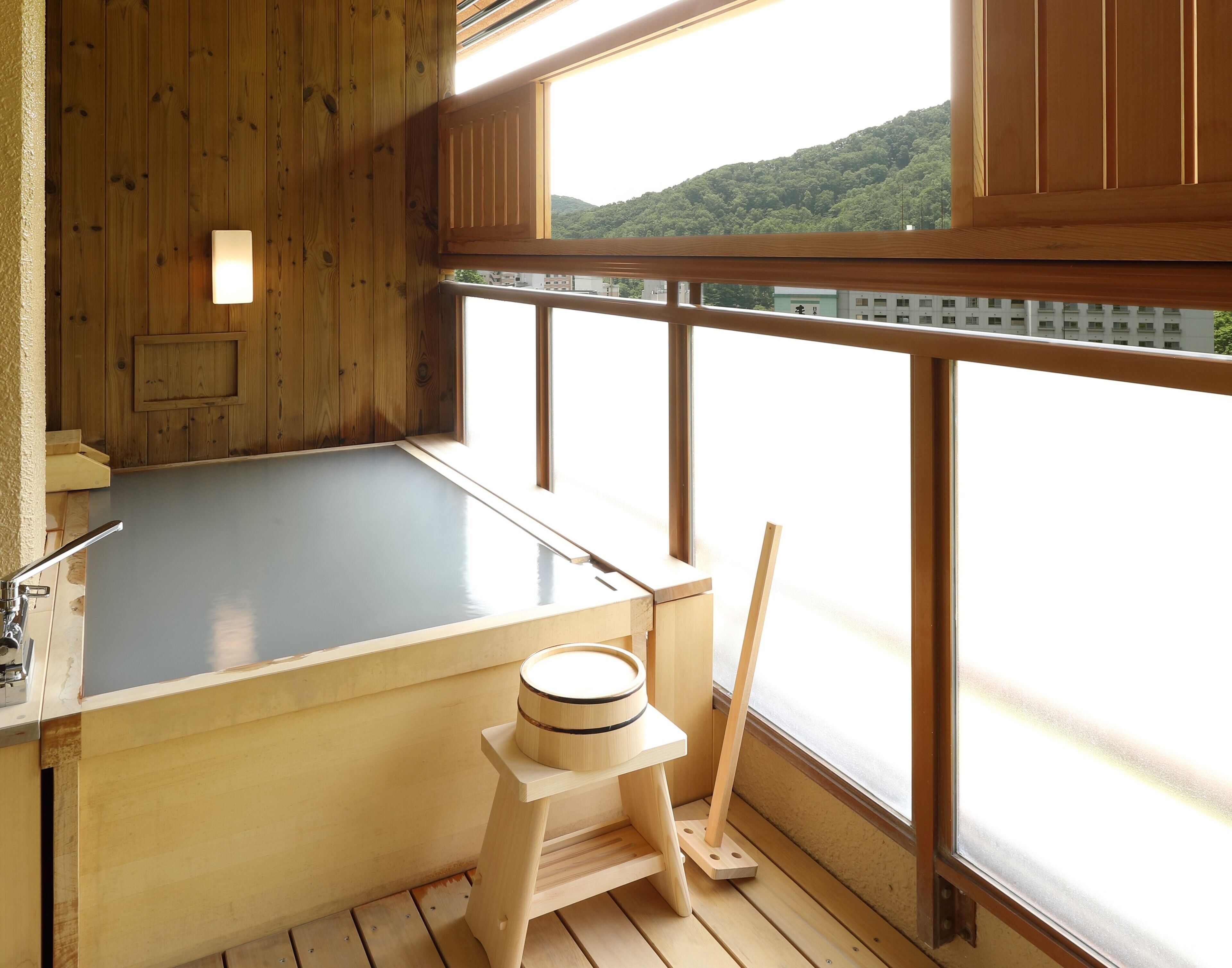 A wooden spa bath with a view of a hill and buildings.