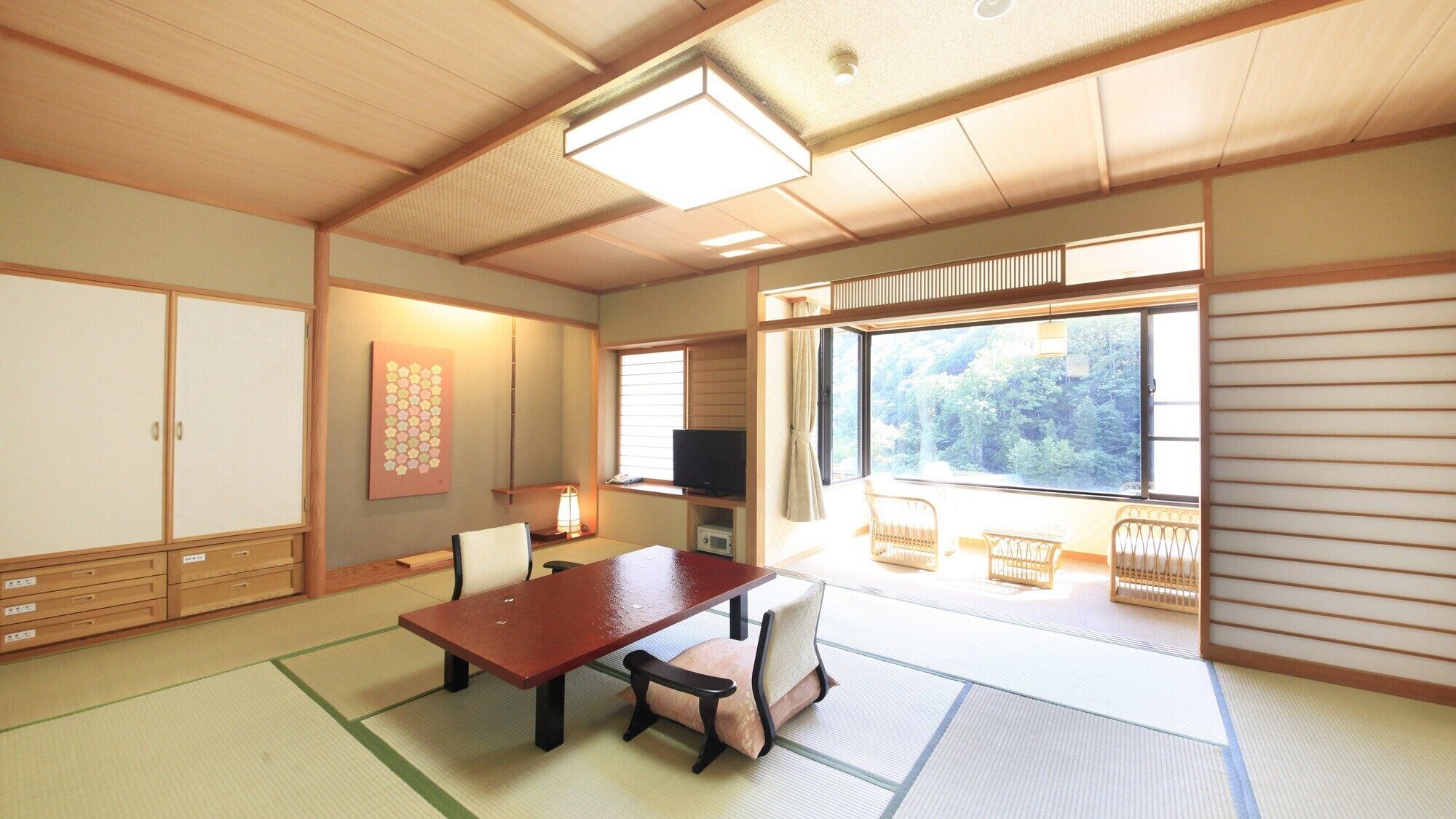 Una habitación japonesa tradicional con suelo de tatami, una mesita baja, un televisor y vistas a un bosque a través de amplios ventanales.