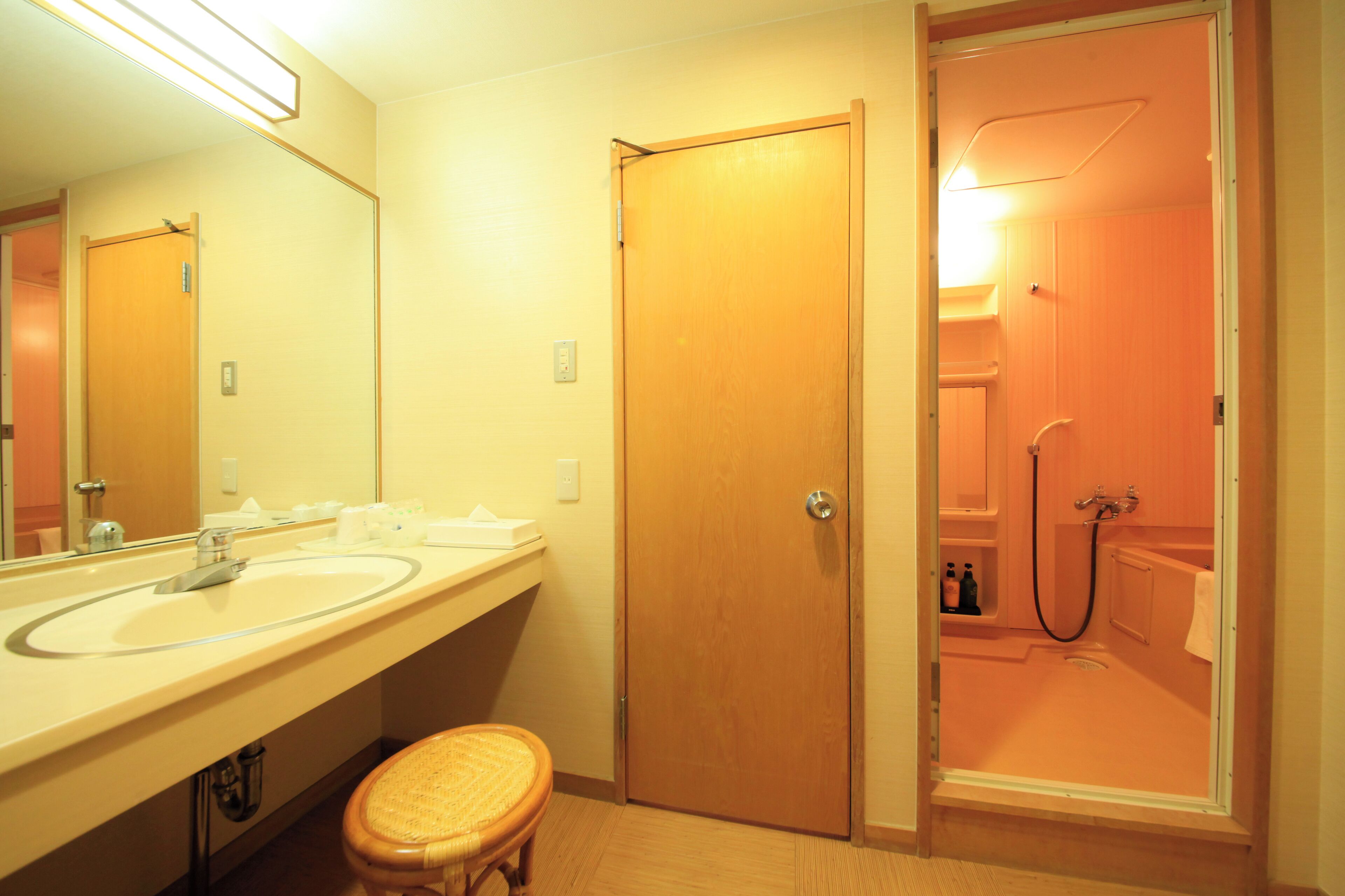 A bathroom with a wooden door, a sink, a mirror, and a shower.