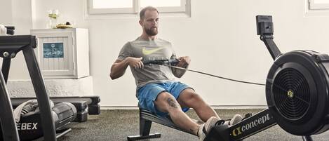 A man using a rowing machine in a gym with a window and a water dispenser in the background.