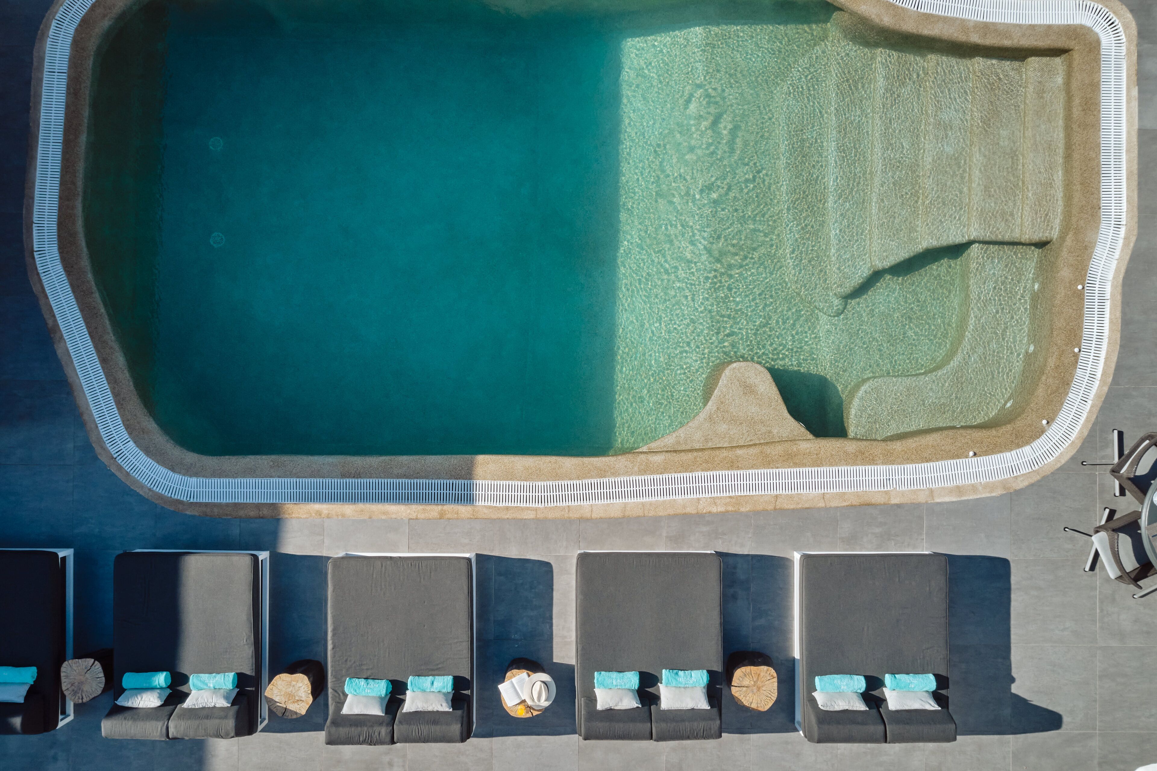 Luftaufnahme eines Schwimmbeckens mit gefliestem Deck und Liegestühlen.