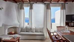 A cozy room with a sofa, a small table, a TV, and a view of the sea. - Mykonos Princess Hotel (Mykonos)