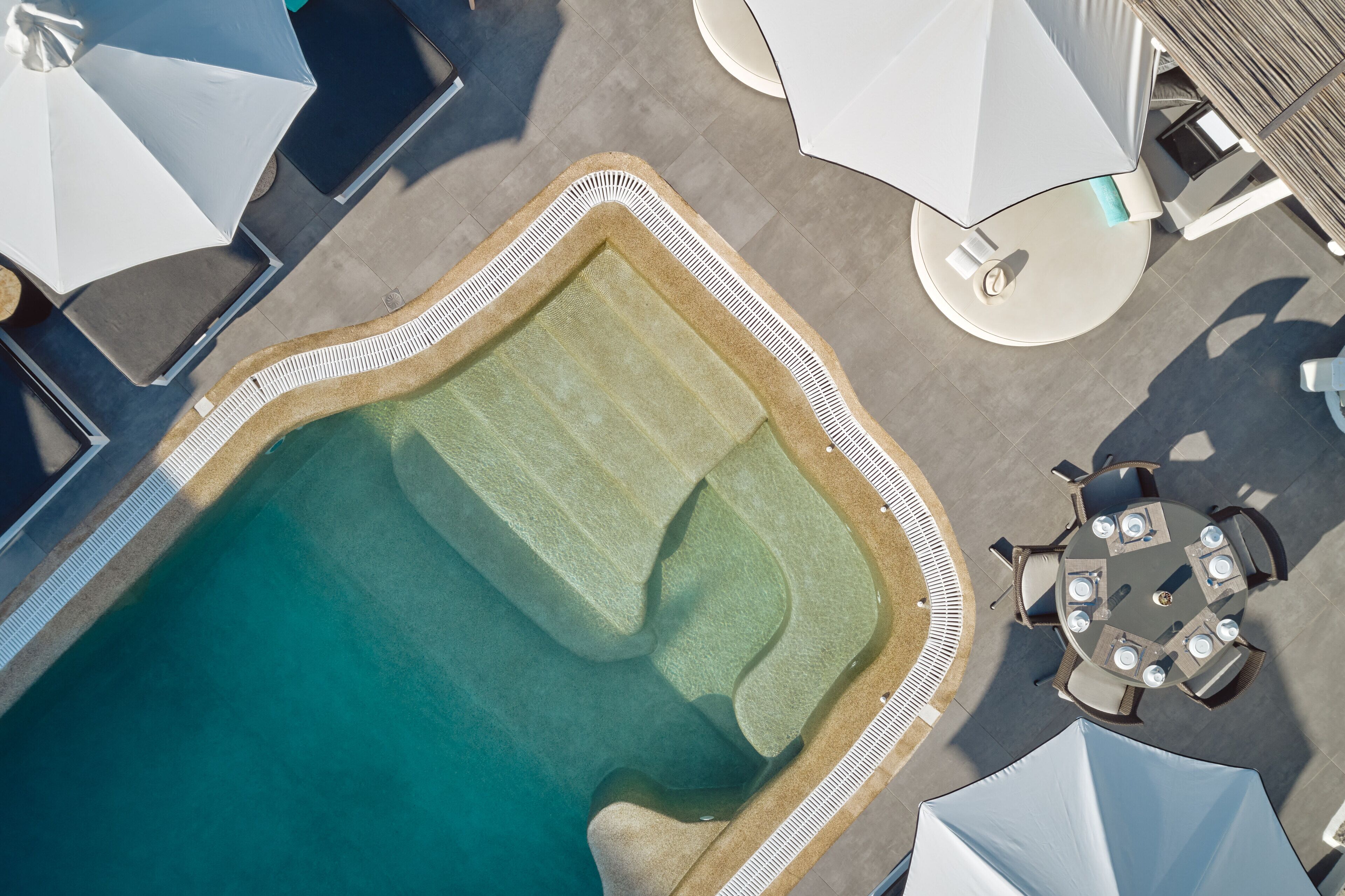 An aerial view of a swimming pool with a surrounding deck, lounge chairs, and umbrellas.