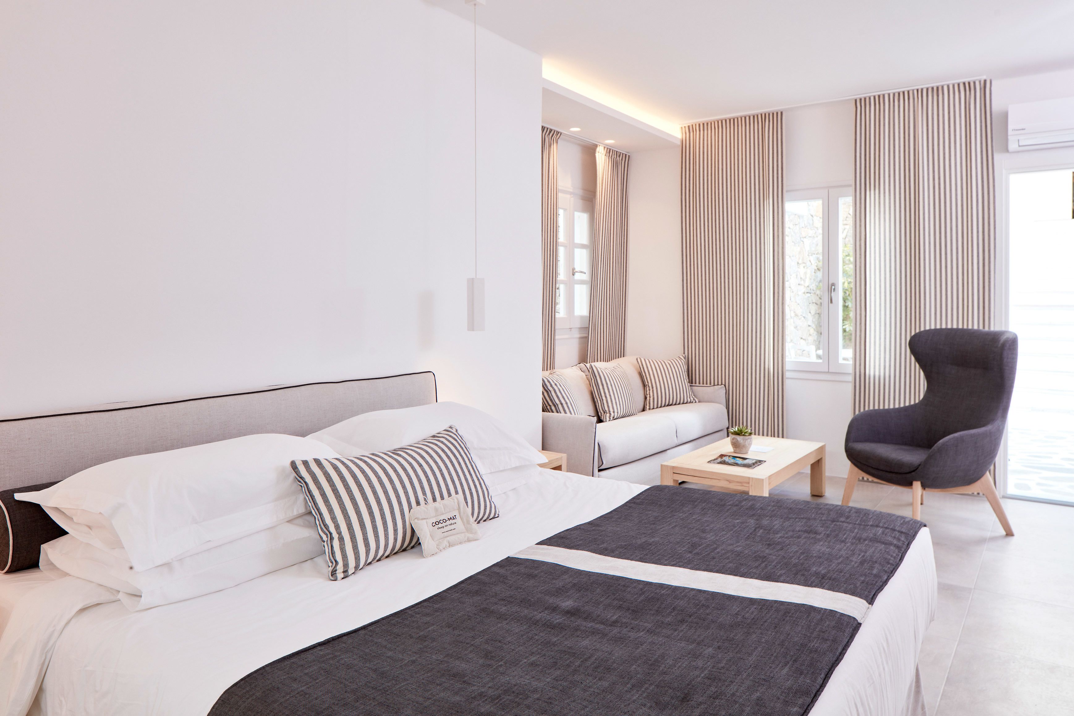 A modern hotel room with a large bed, a sofa, a chair, and a small table.