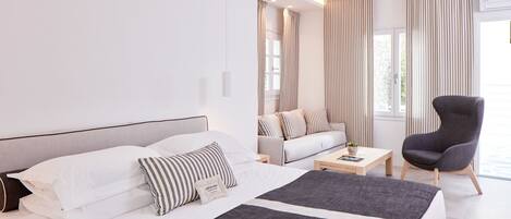 A modern hotel room with a large bed, a sofa, a chair, and a small table.