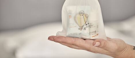 A hand holding a small white drawstring bag with a label that reads "osmè organic baby & me."