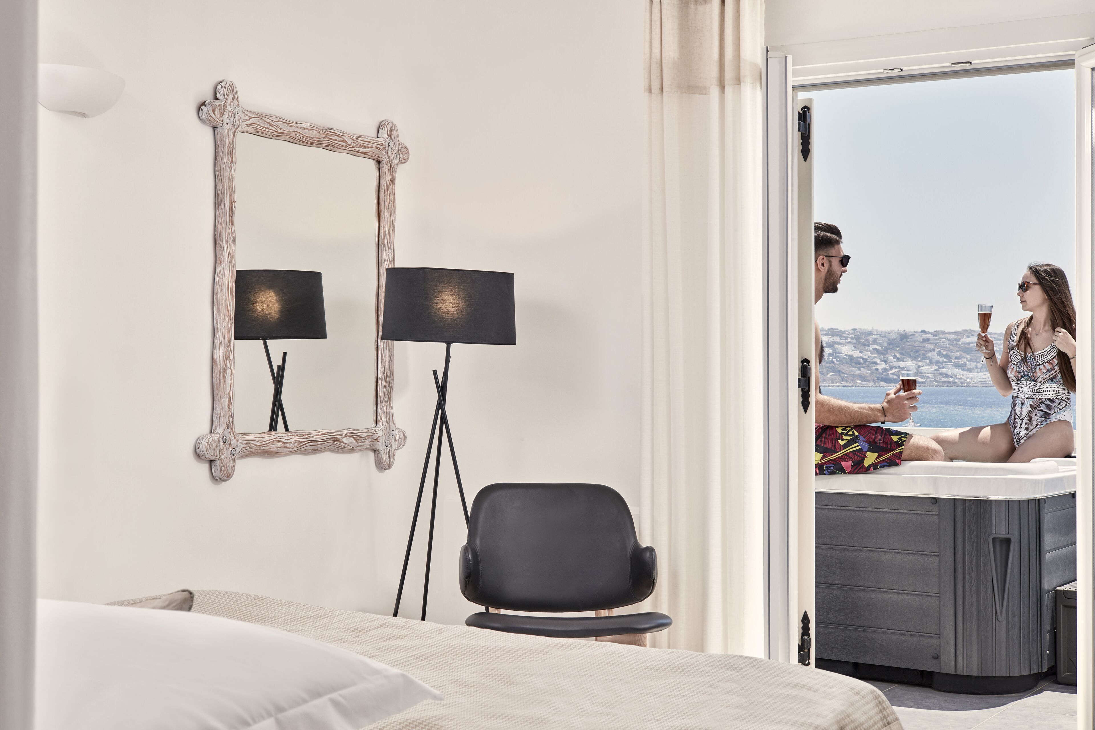 A modern hotel room with a bed, a desk, and a view of the sea.