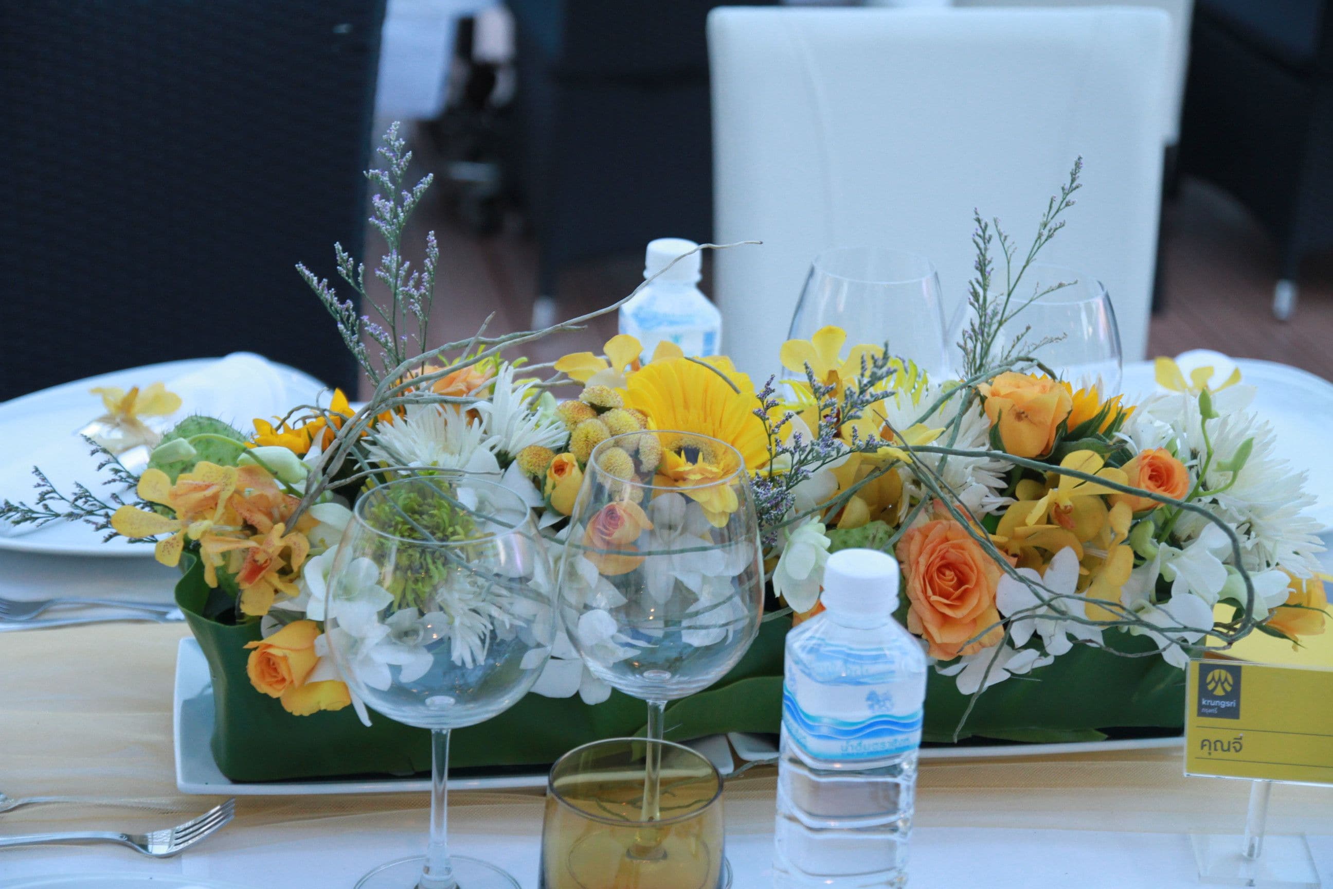 A table set with a floral centerpiece, clear glassware, and a water bottle.