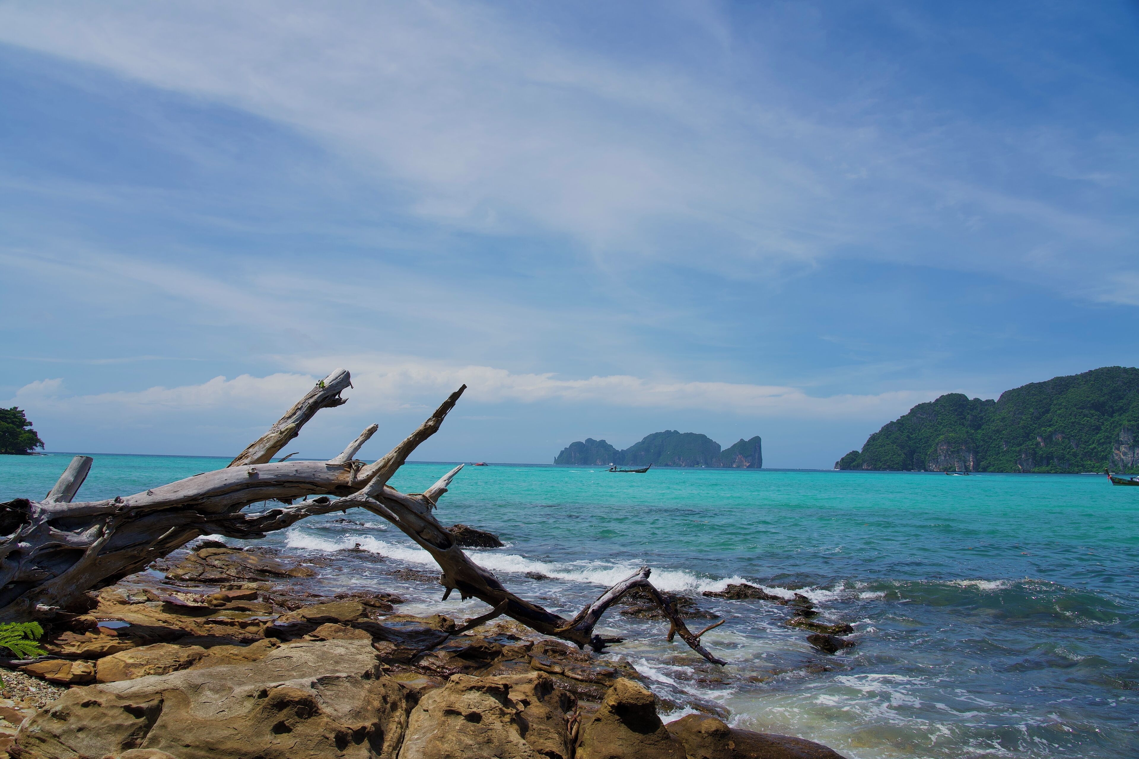 A rocky shoreline with clear turquoise water and distant islands.