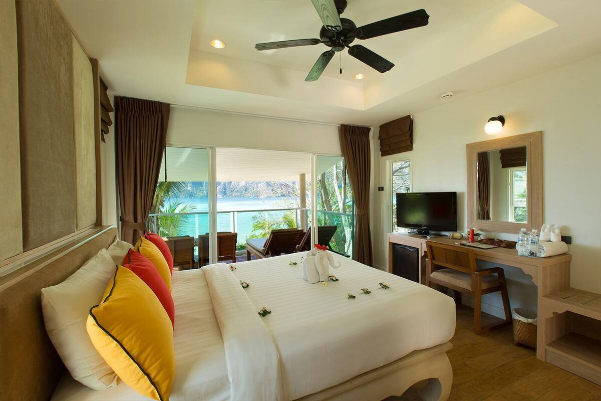 Une chambre d’hôtel avec un lit, un bureau, une télévision et un balcon donnant sur la mer.