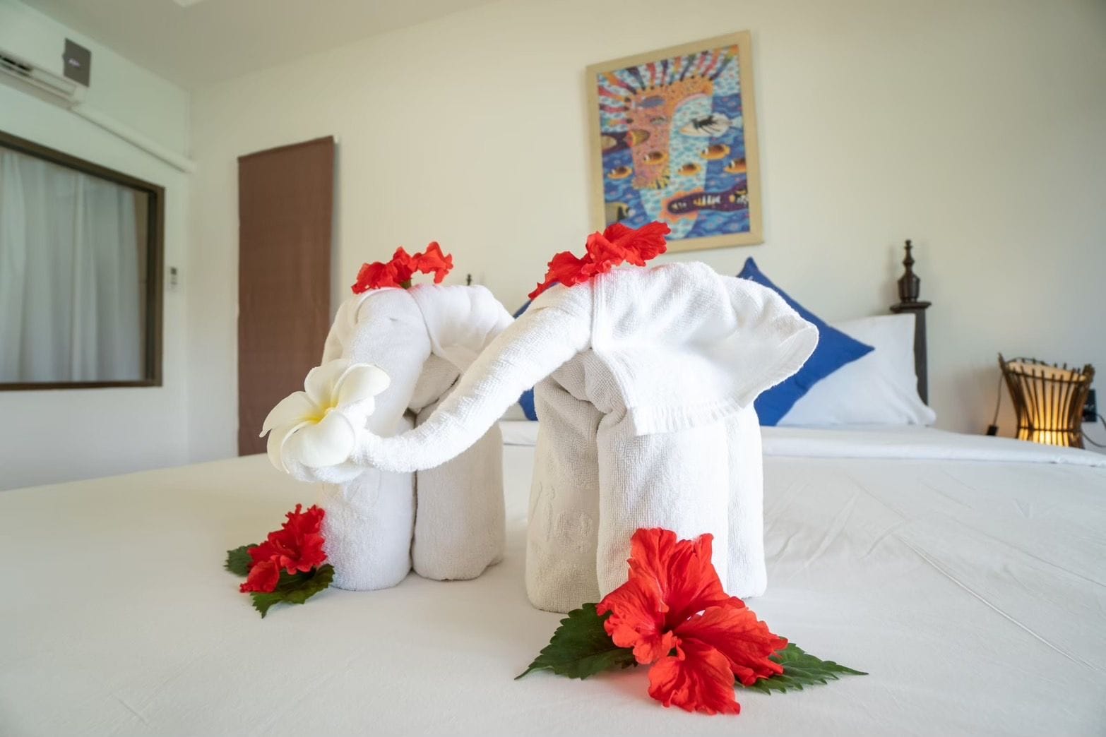 A hotel room with a bed, a painting on the wall, and a decorative towel elephant on the bed.