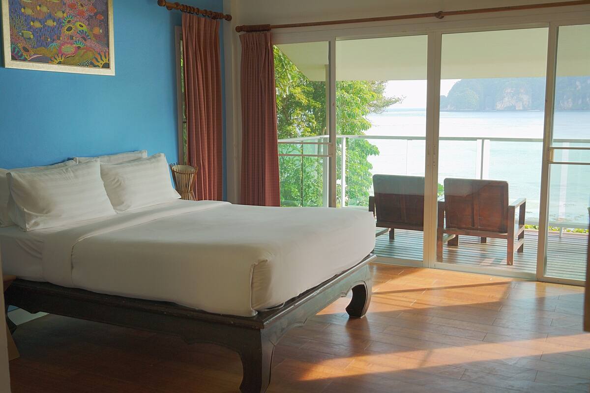 Une chambre avec un grand lit, une vue sur la mer par une porte-fenêtre coulissante et un tableau accroché au mur.