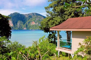 A beachfront property with a covered outdoor seating area overlooking a calm sea and lush greenery.