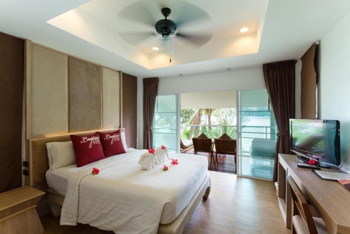 A hotel room with a large bed, a TV, a desk, and a balcony with a view.