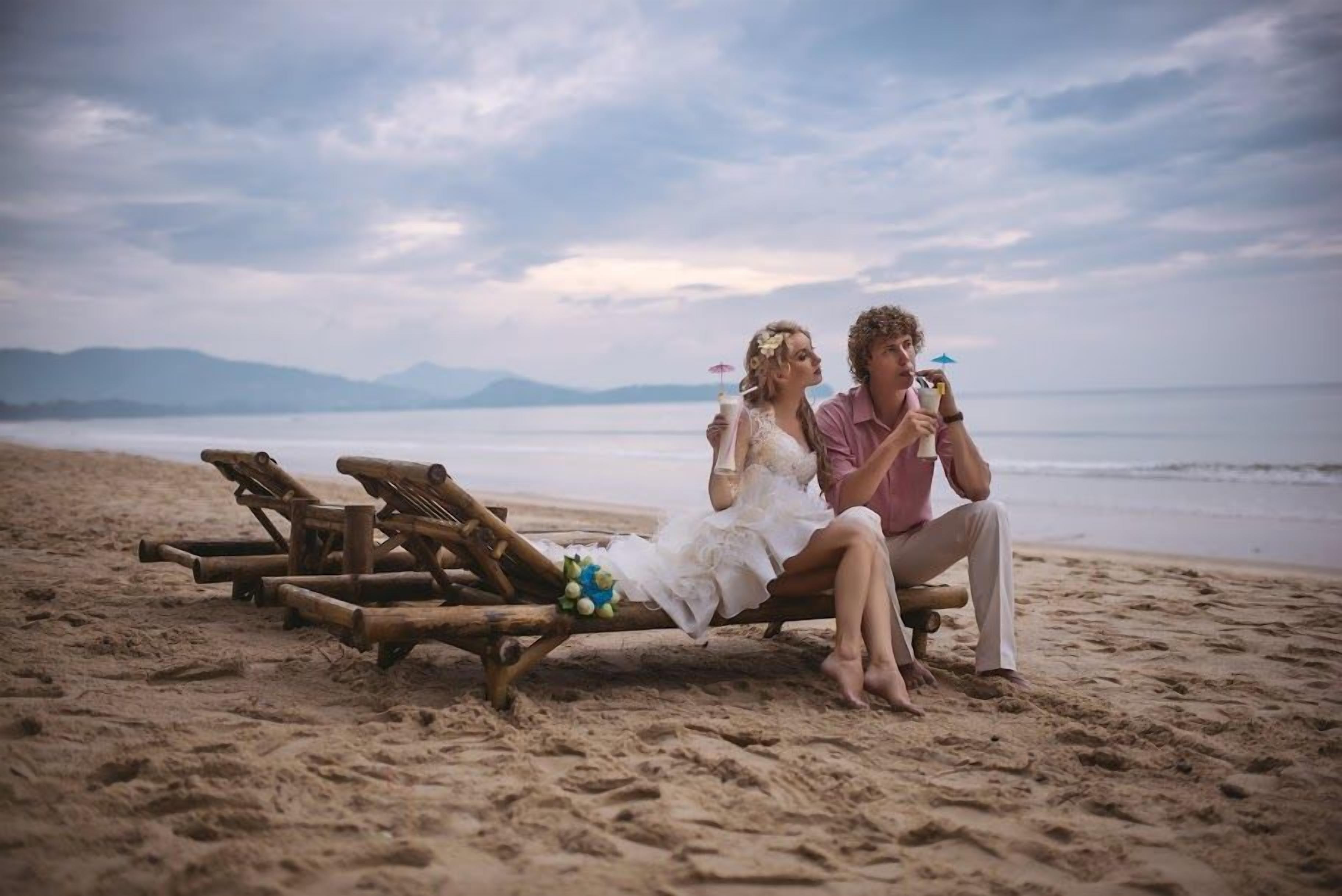Une scène de plage avec des chaises longues en bois et un couple assis sur l’une d’elles.