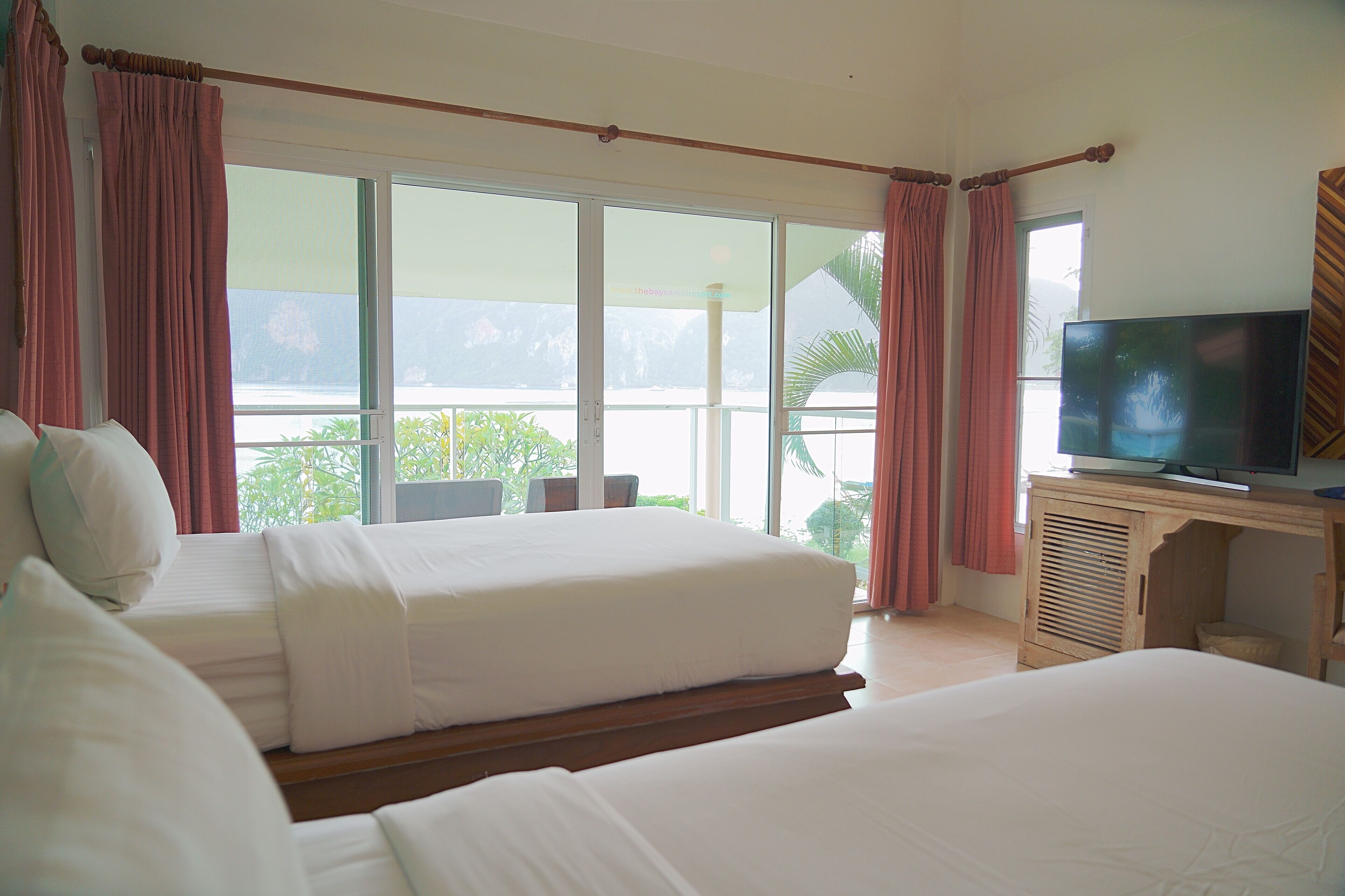 Quarto de hotel com duas camas, televisão e varanda vista para o mar.